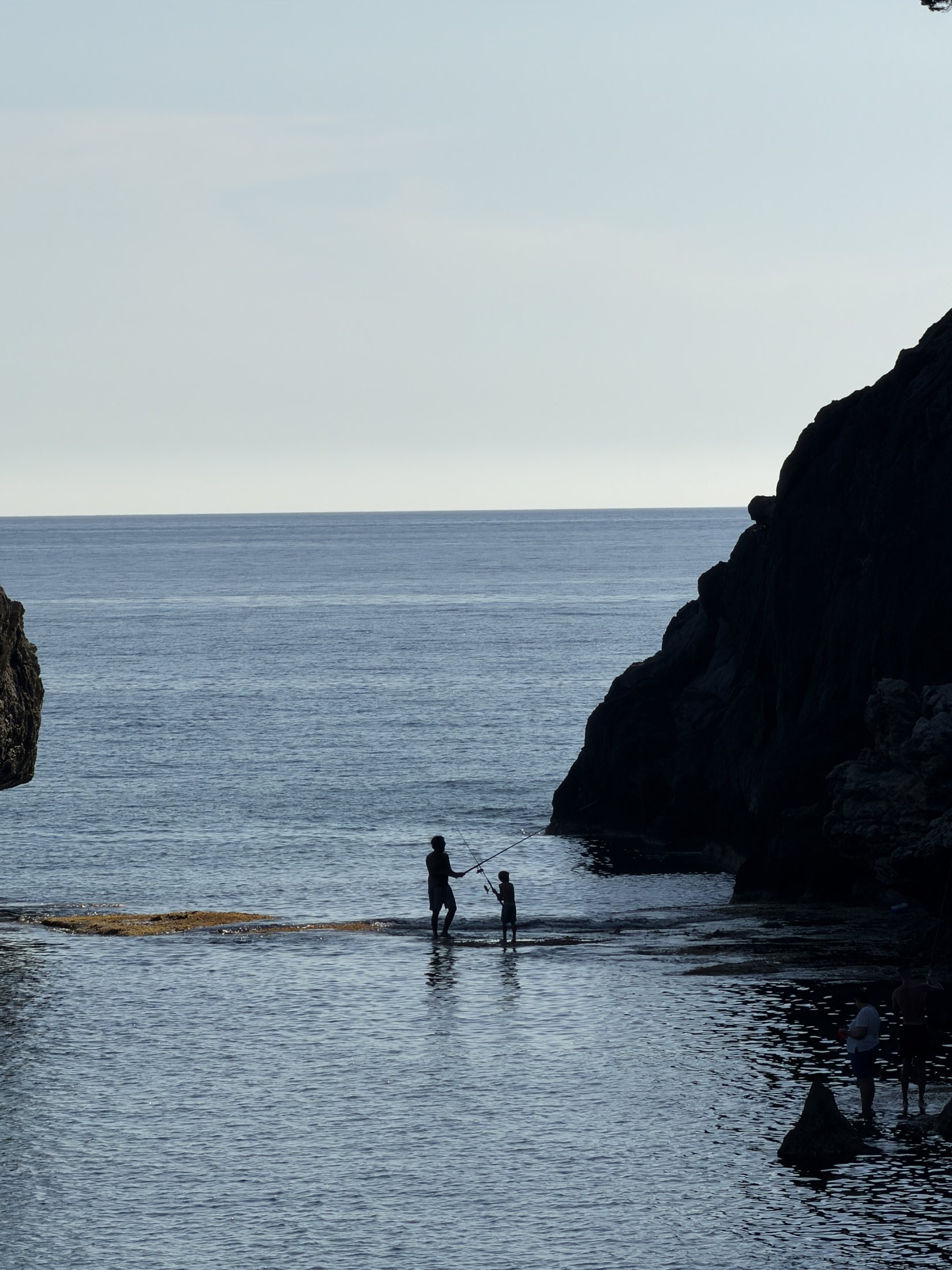 A family fishing together in a quiet Greek cove